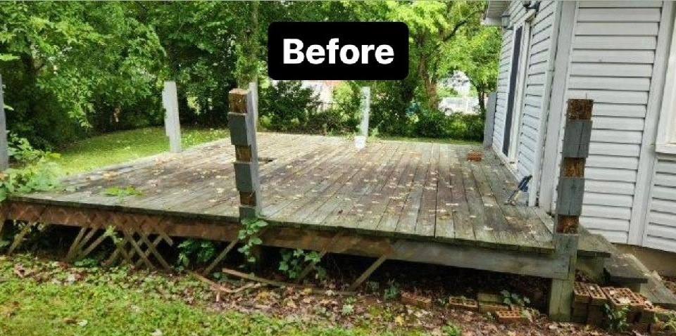 An old timber deck at the back of a house, its boards weathered grey and soft, support posts leaning outward and the lattice skirt beneath it collapsed into fallen leaves.